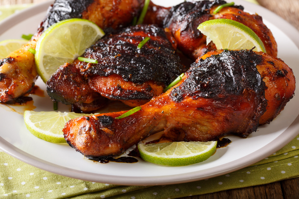 Jamaican food: jerk chicken drumstick with lime closeup on a plate. horizontal